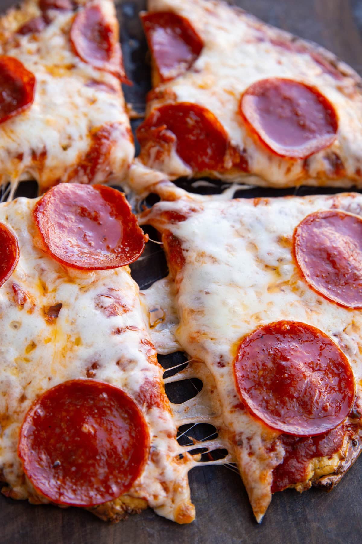 Four slices of pepperoni pizza being pulled apart from one another sitting on a wooden cutting board, ready to serve.