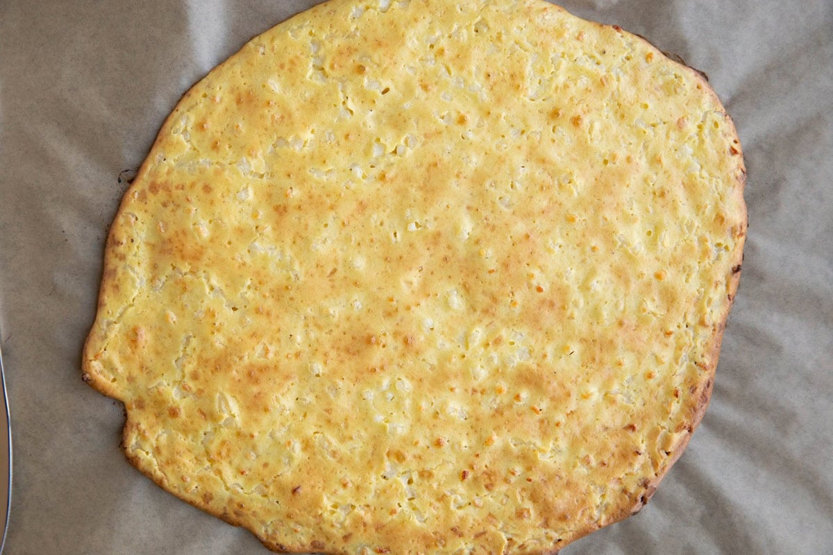 Cottage cheese pizza crust fresh out of the oven on a baking sheet with no toppings on it.