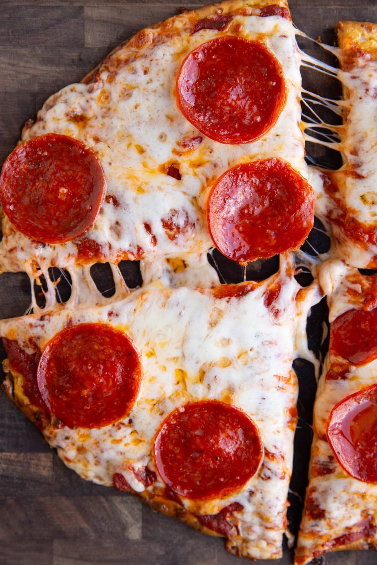Cottage cheese crust pizza sitting on a wooden cutting board cut into four slices with the slices pulled apart for a cheese pull.