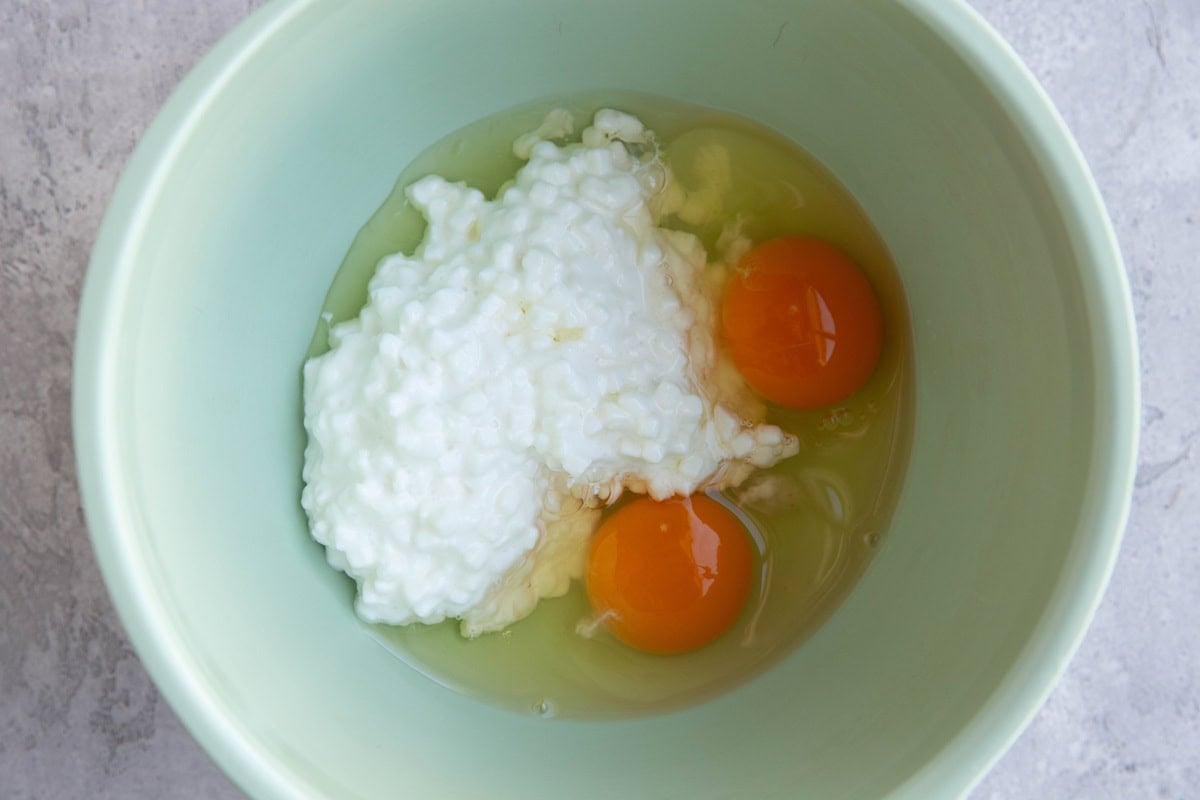 Mixing bowl of cottage cheese and two eggs, ready to be mixed together.