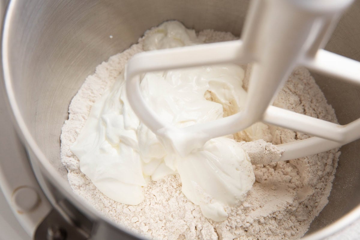 Stand mixer with dry ingredients on the bottom and a white creamy substance (cottage cheese) on top.