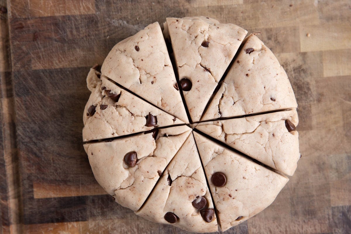 Chocolate chip scone dough cut into 8 triangles on a wooden cutting board.