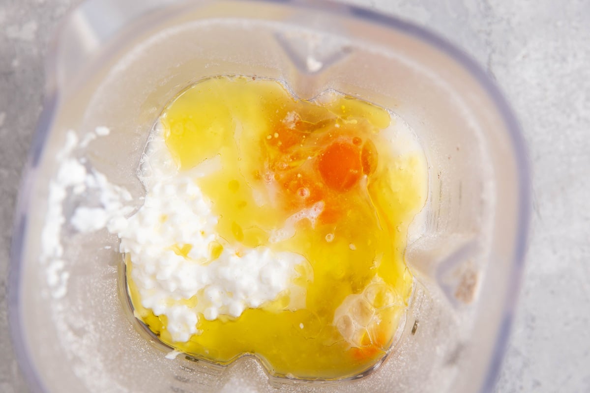Blender with eggs, oil, cottage cheese, and oat flour inside, ready to be blended into waffle batter.