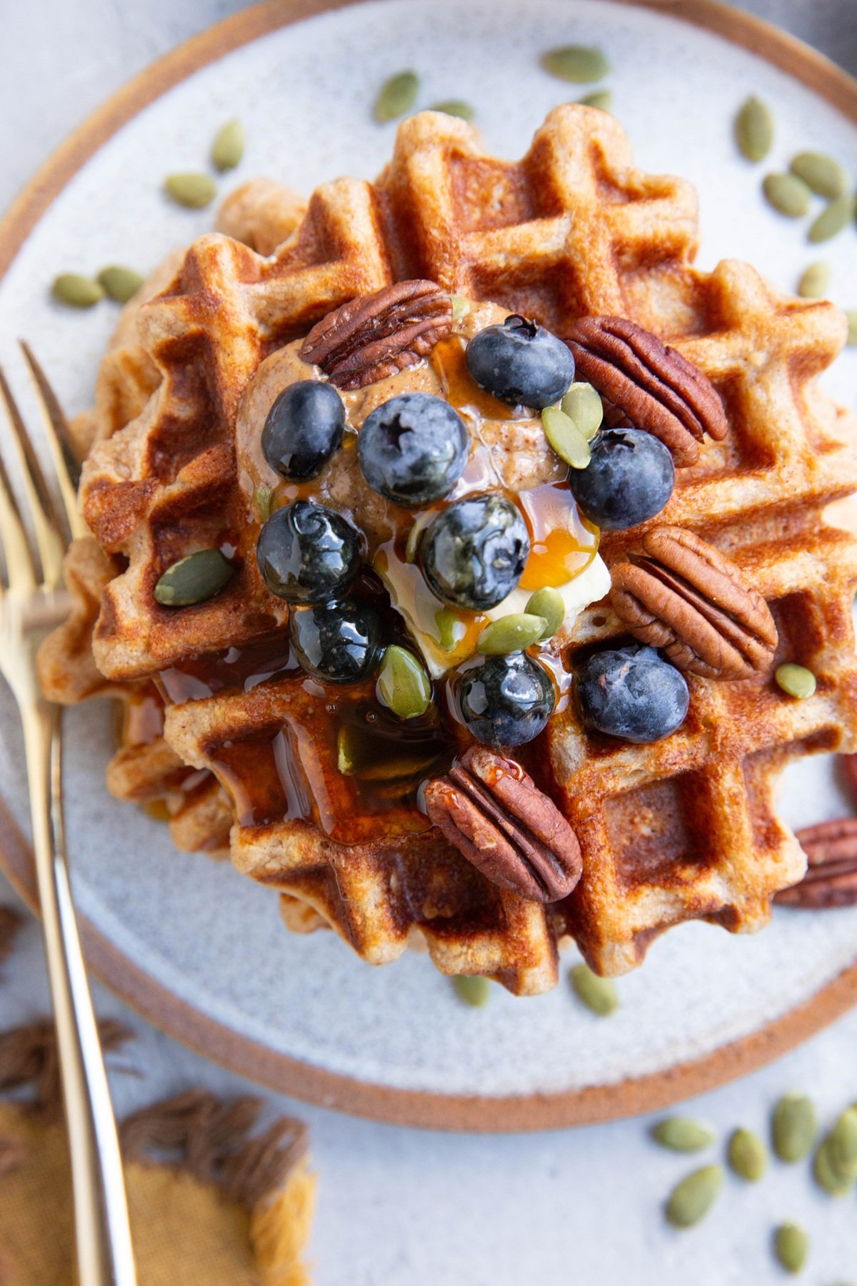 Waffles with butter, almond butter, blueberries, pecans and pumpkin seeds on top.