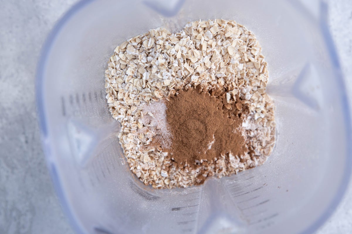 Blender full of oats, cinnamon, baking powder, and salt, ready to be blended into a flour.