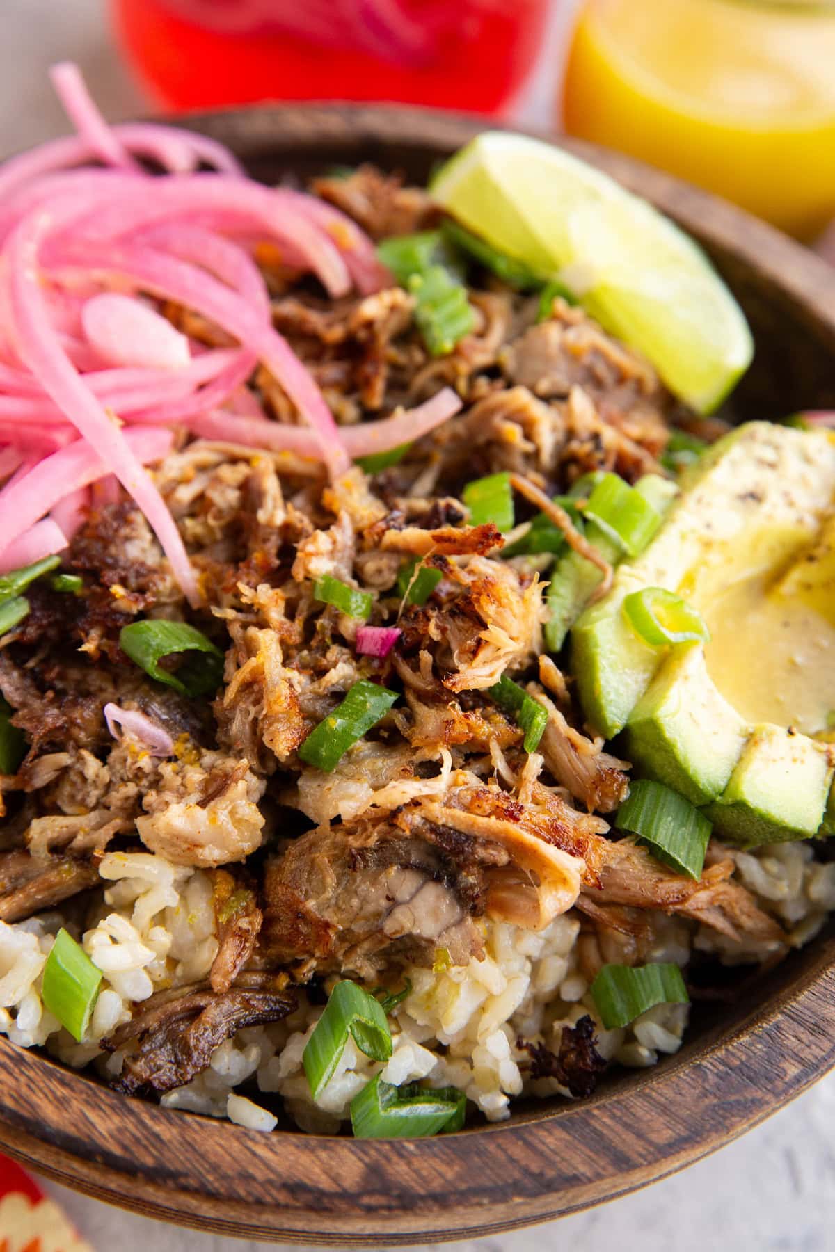 Crispy shredded pork in a bowl of brown rice with sliced avocado, pickled onions, and mojo sauce drizzled on top.