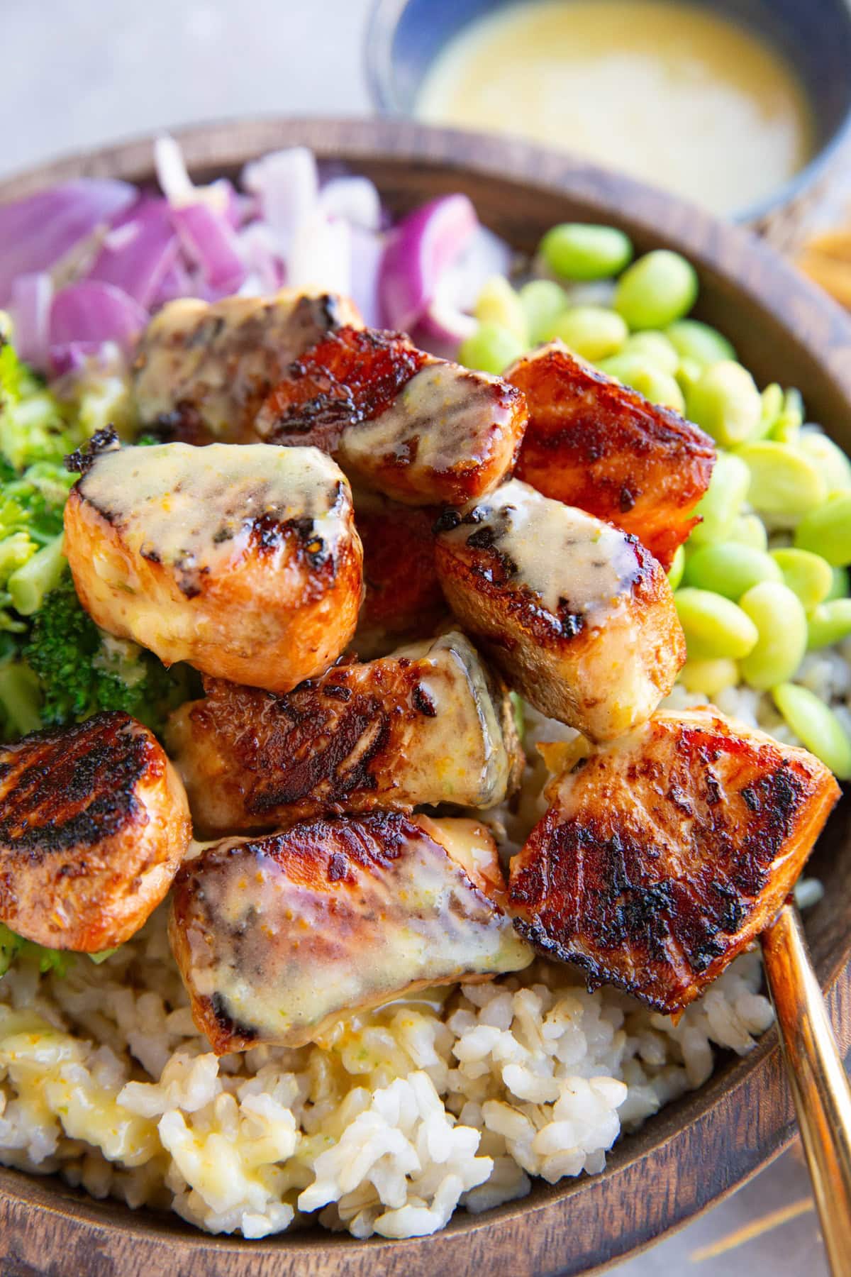 Mojo salmon bites in a bowl full of rice, edamame, red onion, and broccoli drizzled with mojo sauce.