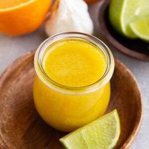 Jar of Mojo sauce with oranges, limes and garlic in the background.