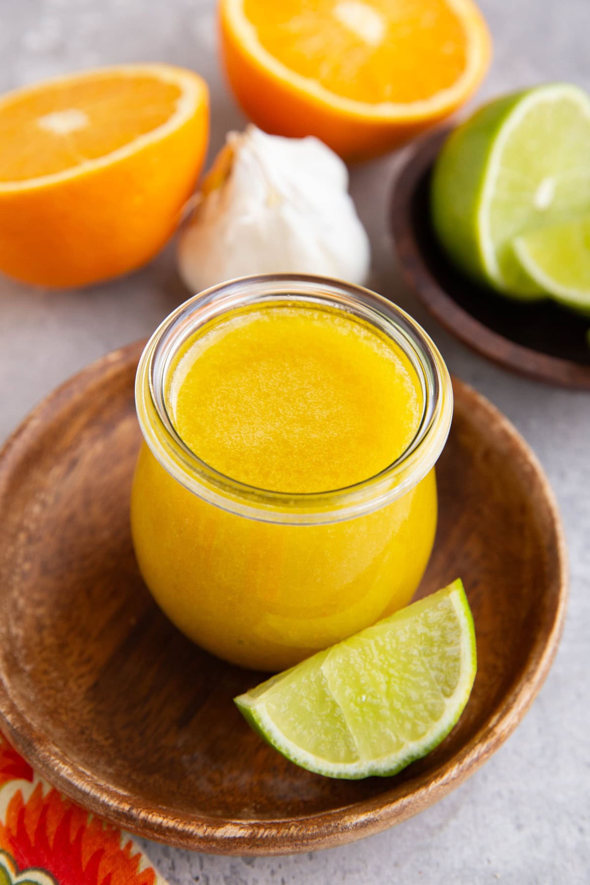 Jar of Mojo sauce with oranges, limes and garlic in the background.