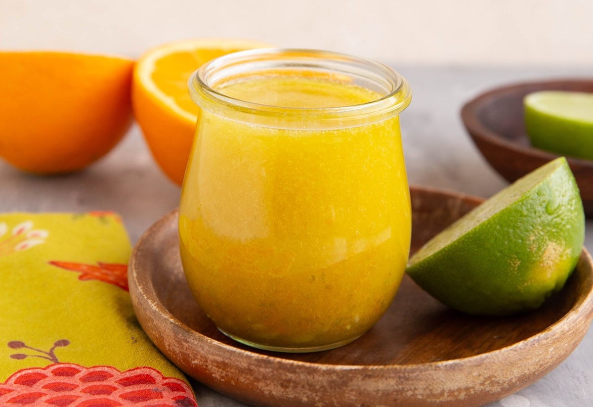 Mojo sauce in a small jar with fresh limes and oranges in the background