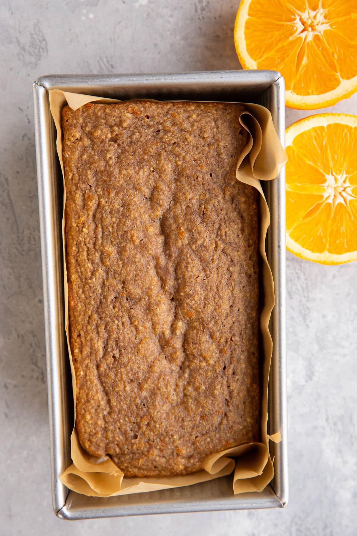 Loaf pan with orange loaf inside and a fresh orange sliced in half to the side.