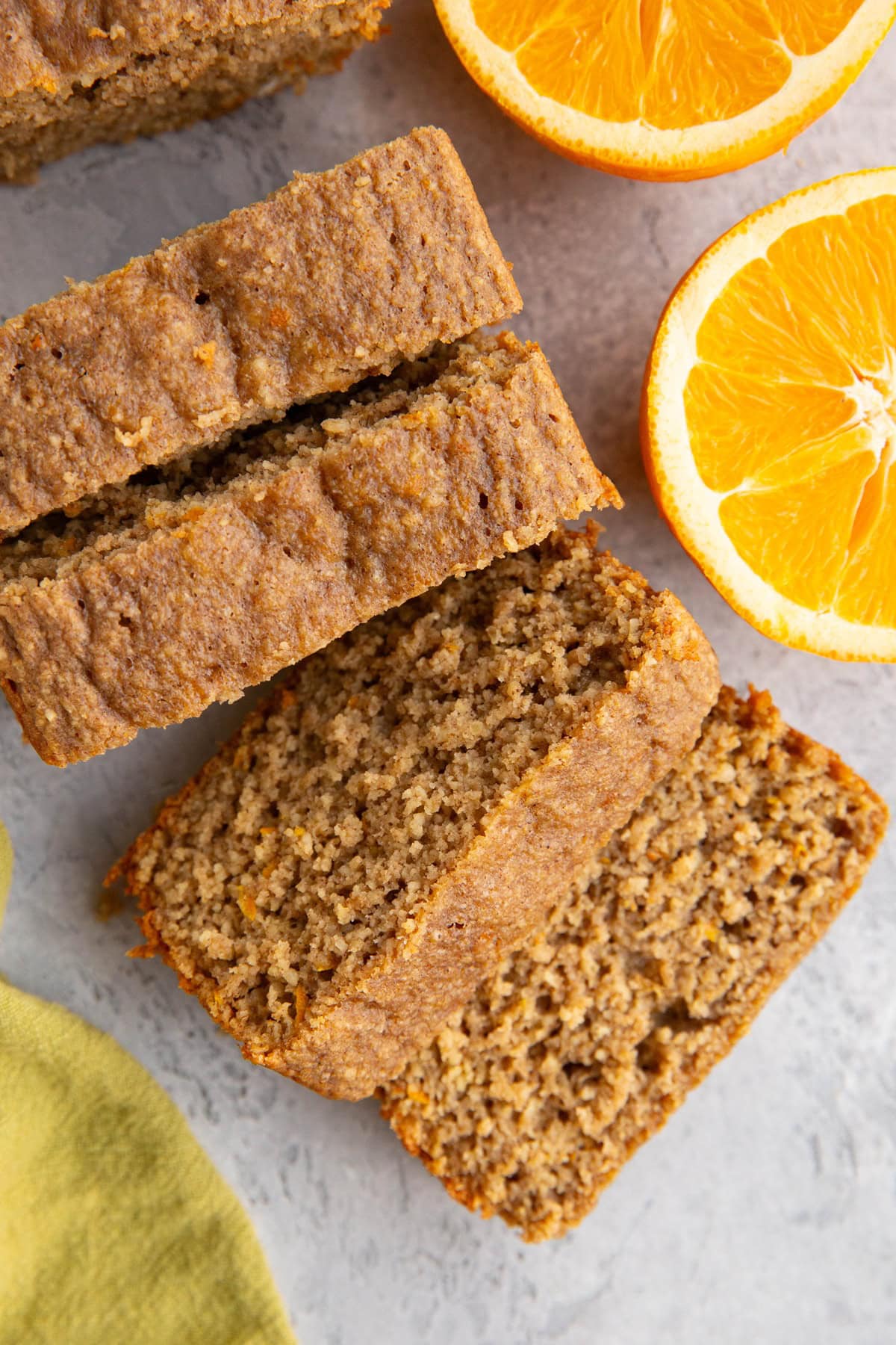 Orange loaf cut into slices with a fresh orange sliced in half to the side and a green napkin.