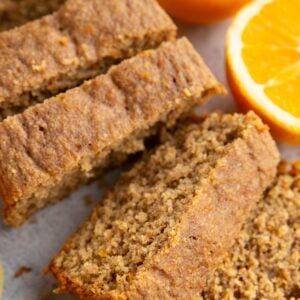 Orange loaf cut into individual slices with a fresh orange sliced in half to the side.