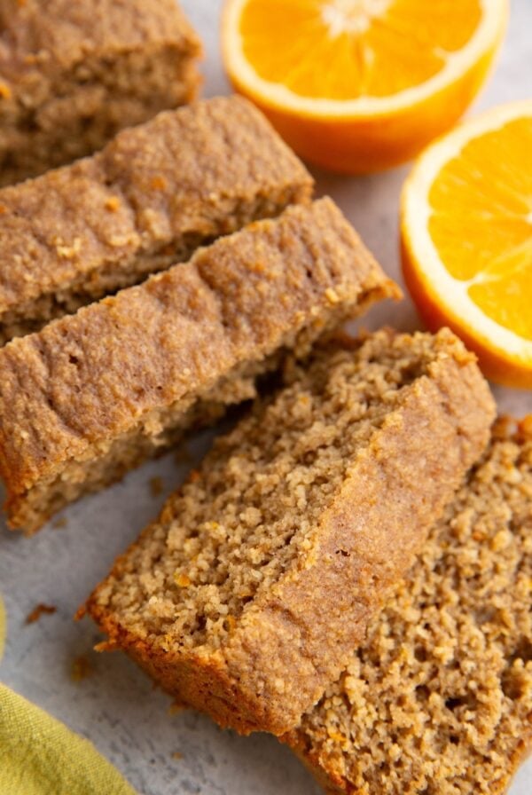 Orange loaf cut into individual slices with a fresh orange sliced in half to the side.