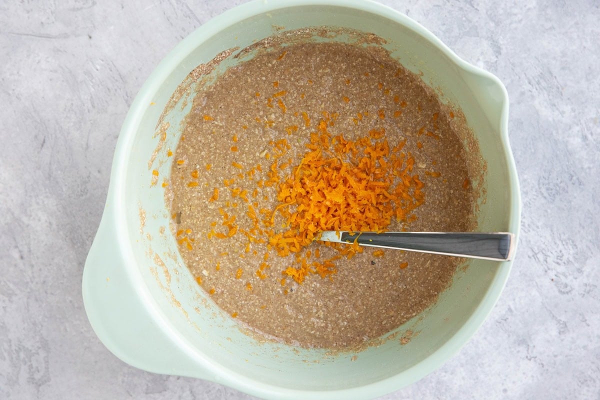 Mixing bowl full of oatmeal bread batter with orange zest on top, ready to be mixed in.