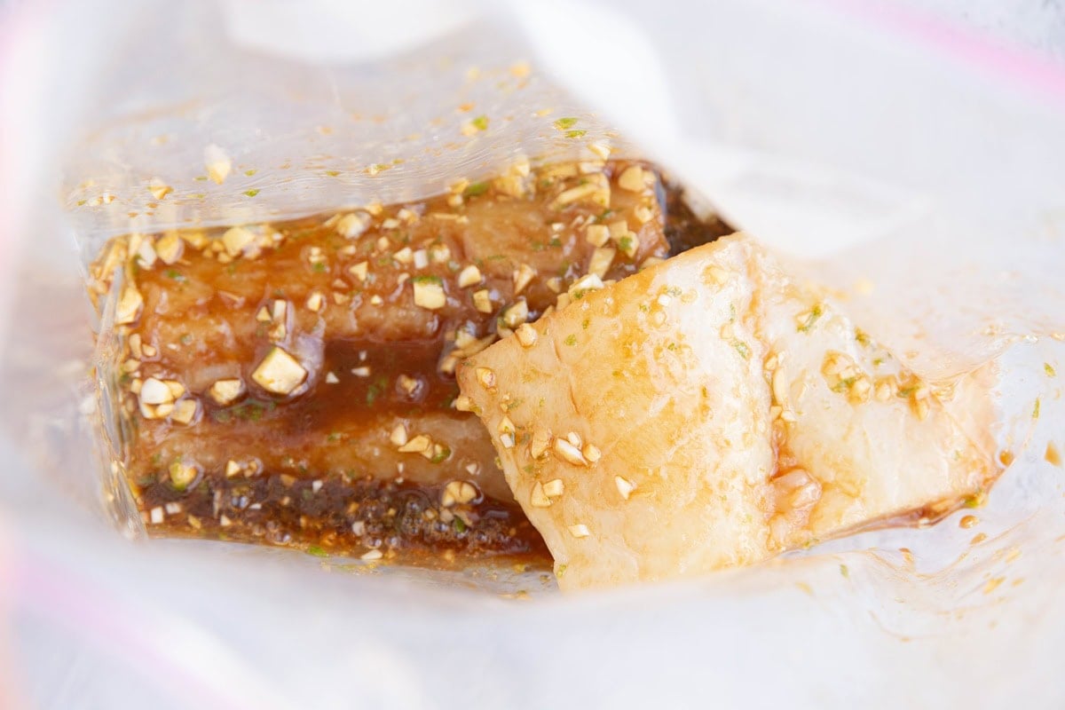 Raw cod filets in a large zip lock bag with marinade, ready to marinate in the refrigerator.