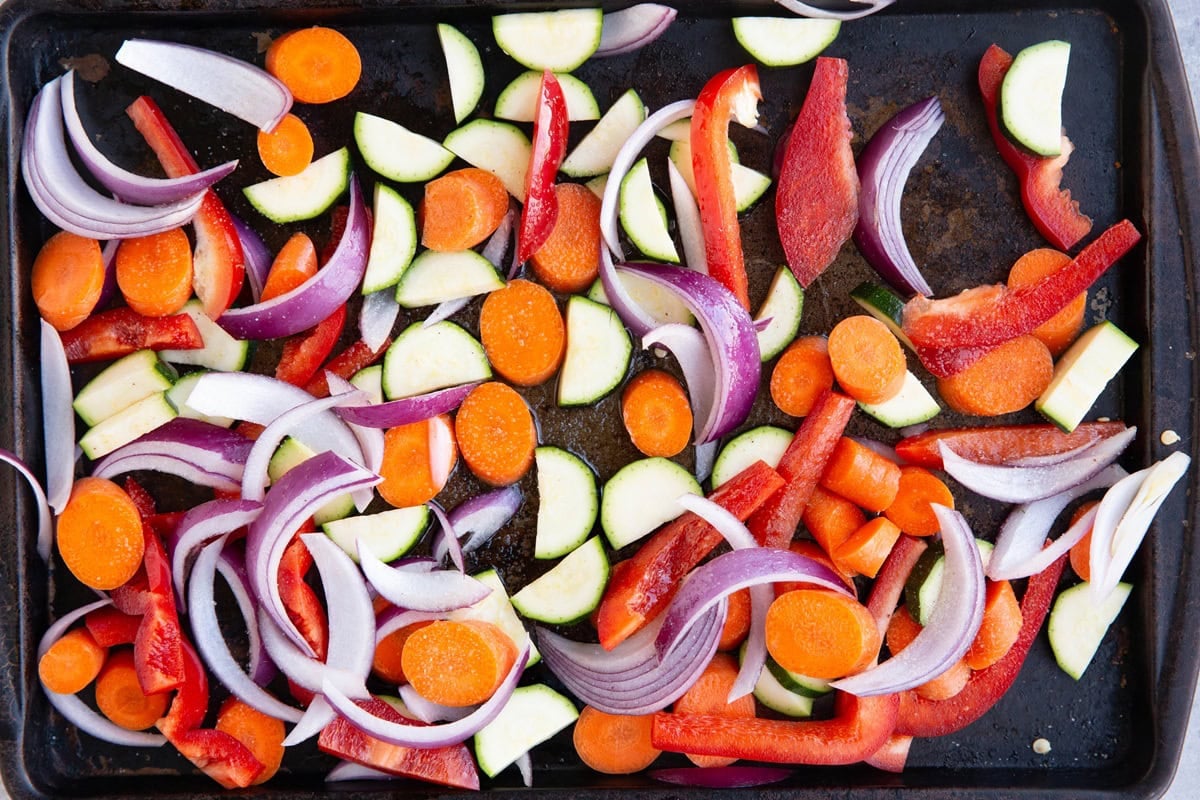 Sheet pan with chopped vegetables coated in oil and sea salt spread in an even layer.