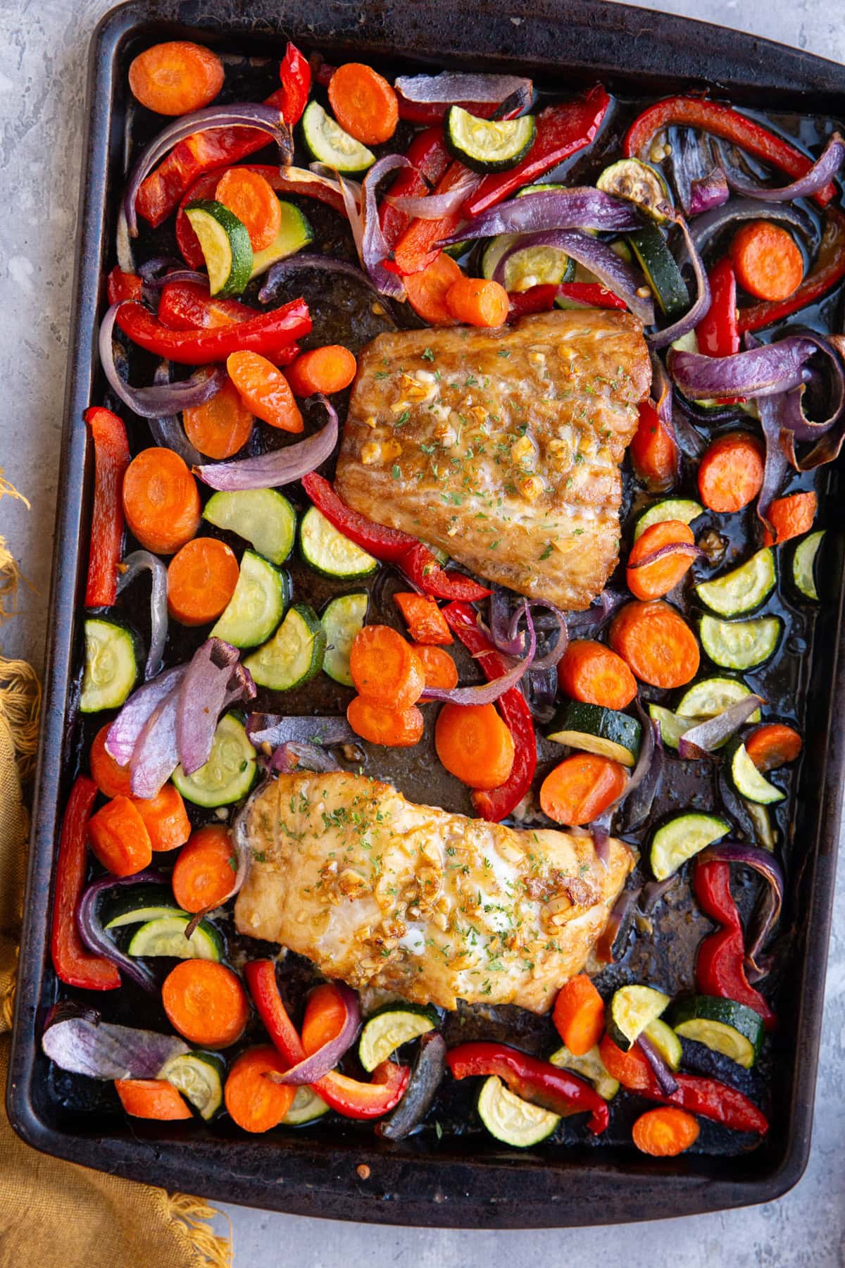 Sheet pan with two cod filets and roasted vegetables, fresh out of the oven and ready to serve for dinner.