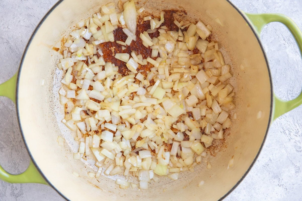 Dutch oven with onions cooking inside bacon fat.