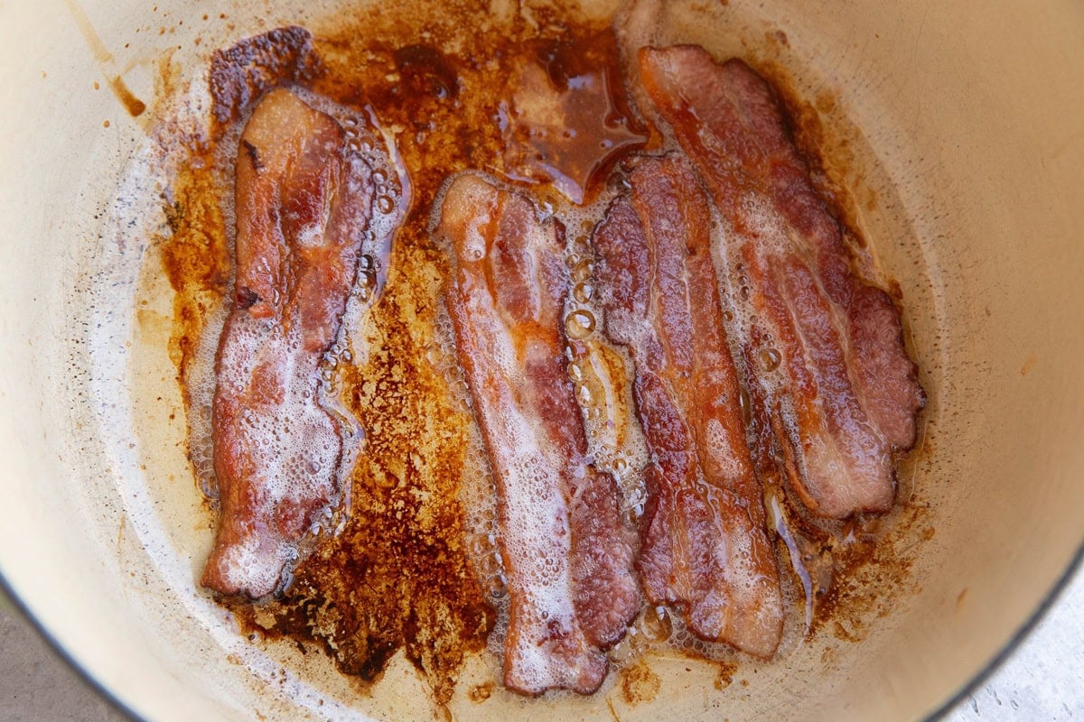 Bacon cooking inside of a large pot.