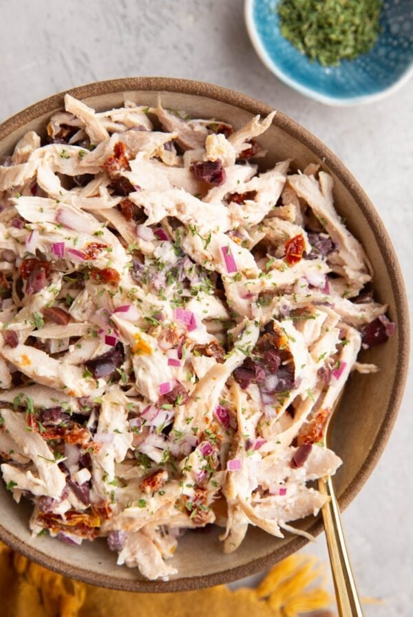 Large ceramic bowl full of Mediterranean Rotisserie Chicken Salad with a gold spoon and a gold napkin.
