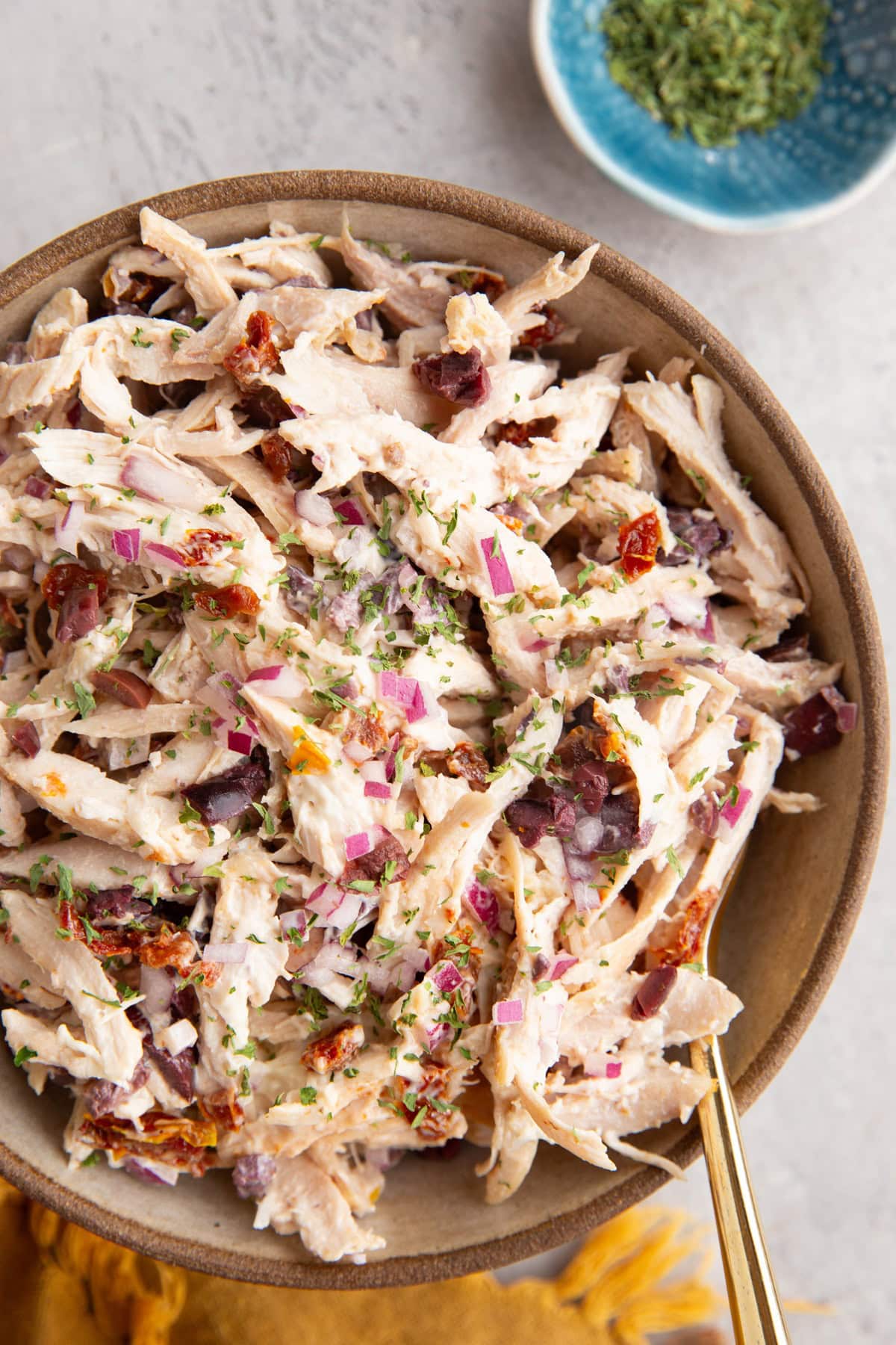 Large ceramic bowl full of Mediterranean Rotisserie Chicken Salad with a gold spoon and a gold napkin.