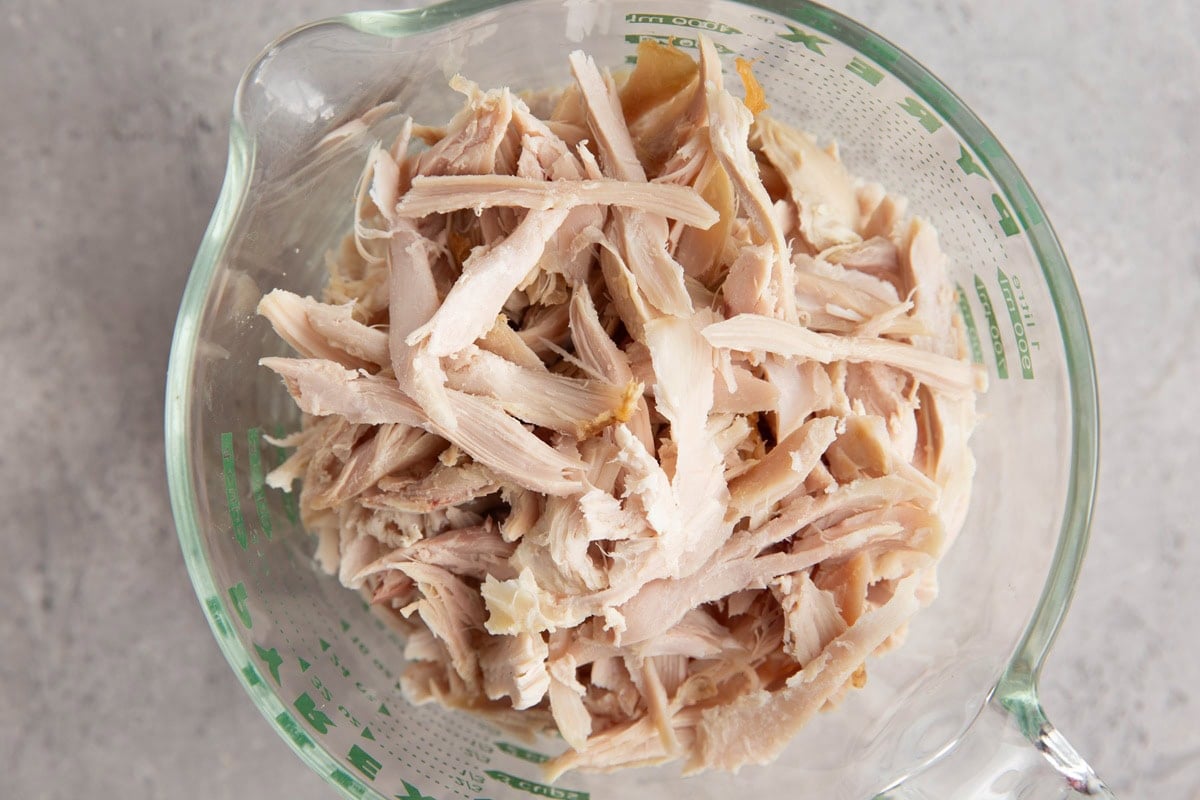 Shredded rotisserie chicken in a large measuring cup to measure out four cups worth.