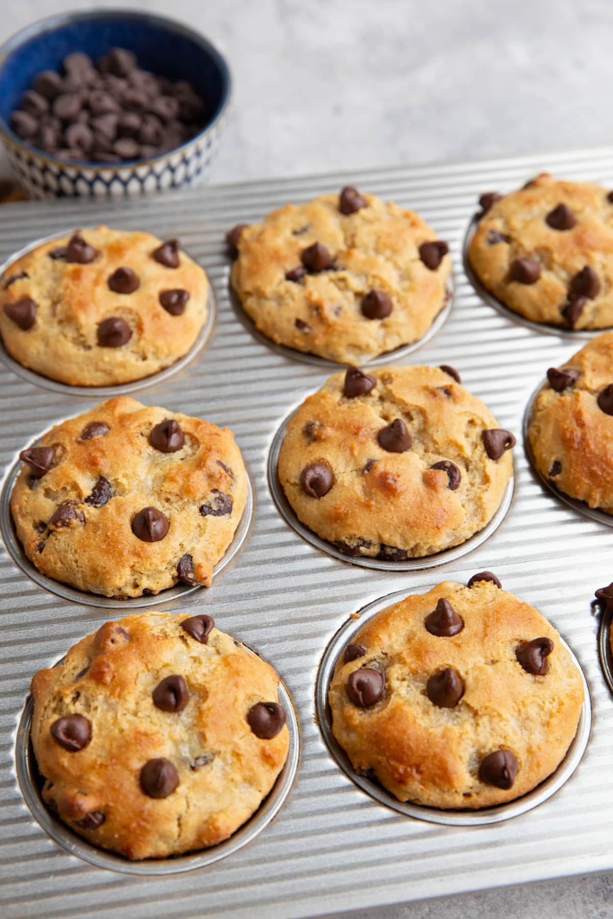 Muffin tray with chocolate chip muffins and chocolate chips in a bowl in the background.