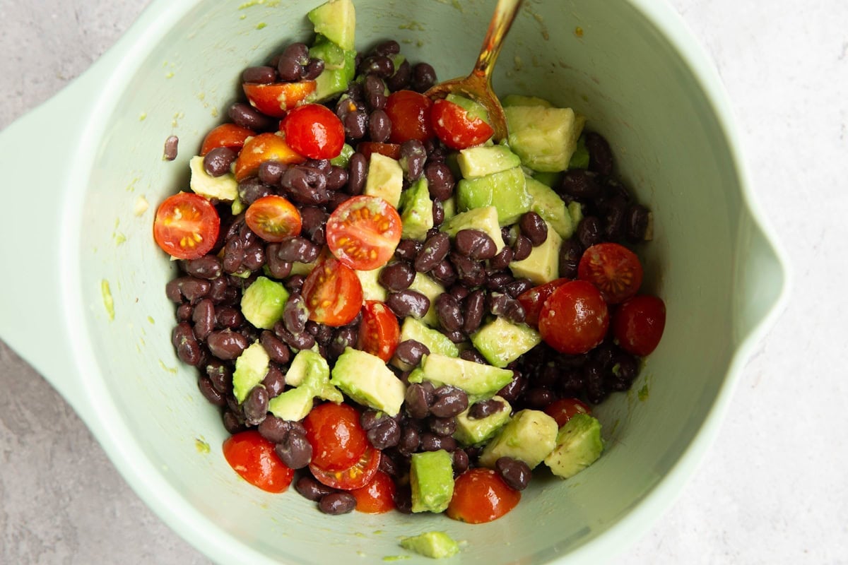 Mixing bowl full of black bean and avocado salad, tossed together in dressing and ready to serve.