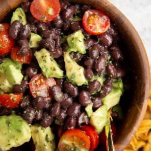 Black Bean and Avocado Salad in a wooden bowl with a gold spoon and a golden napkin to the side.