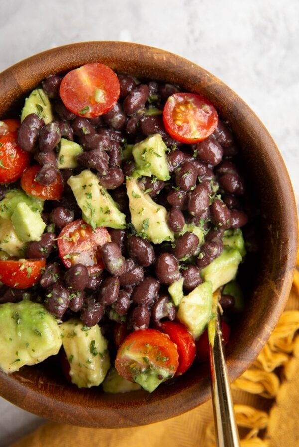 Black Bean and Avocado Salad in a wooden bowl with a gold spoon and a golden napkin to the side.