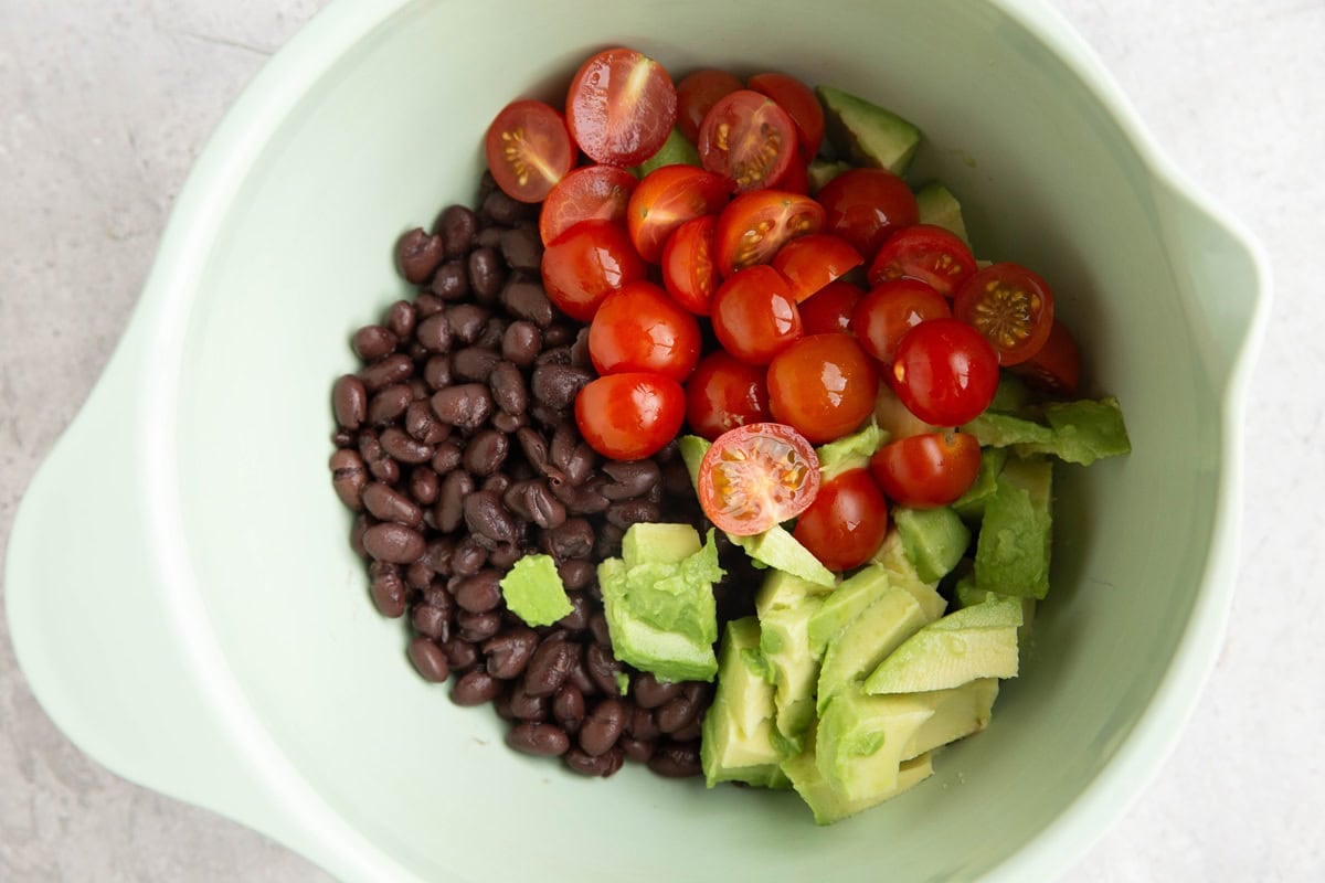 Black beans, tomato, and chopped avocado in a mixing bowl.