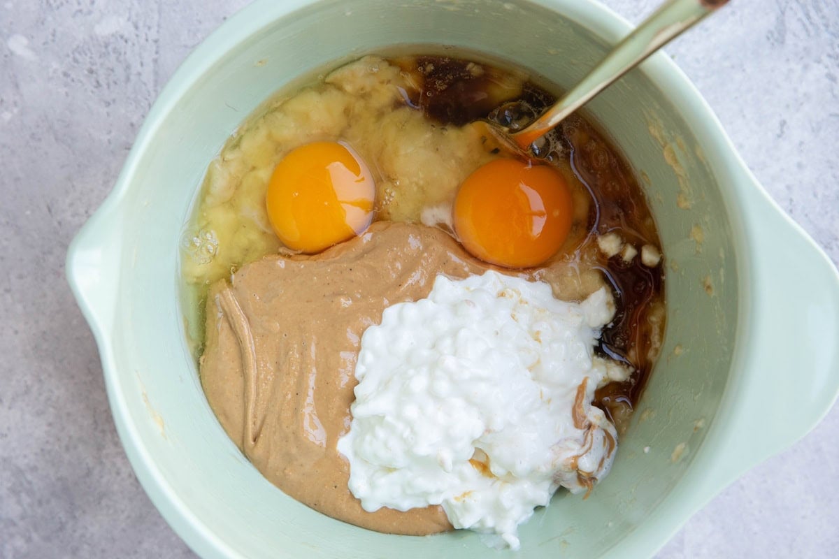 Mixing bowl with mashed banana, eggs, pure maple syrup, cashew butter and cottage cheese