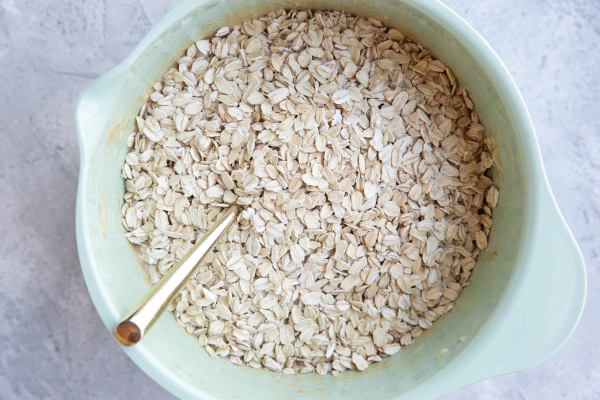 Mixing bowl full of wet ingredients on the bottom and oats on top, ready to be mixed together.