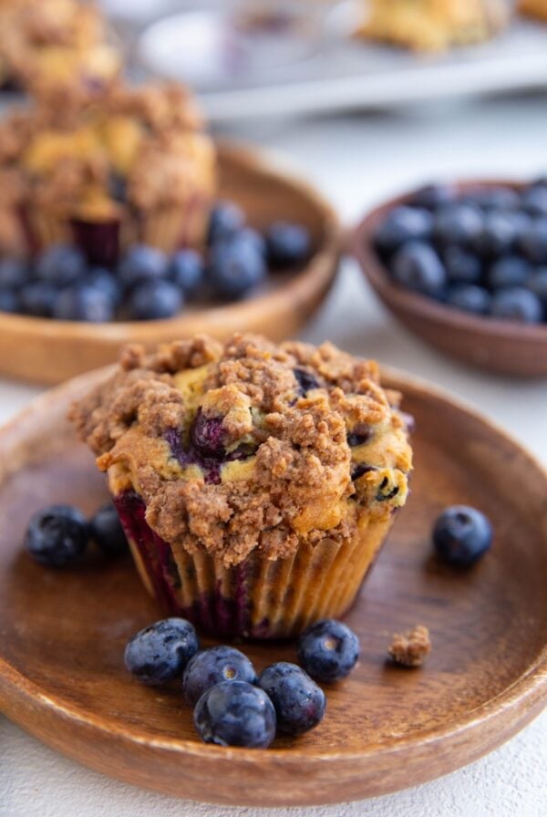 Two wooden plates with blueberry buttermilk muffins and fresh blueberries. A bowl of fresh blueberries in the background.