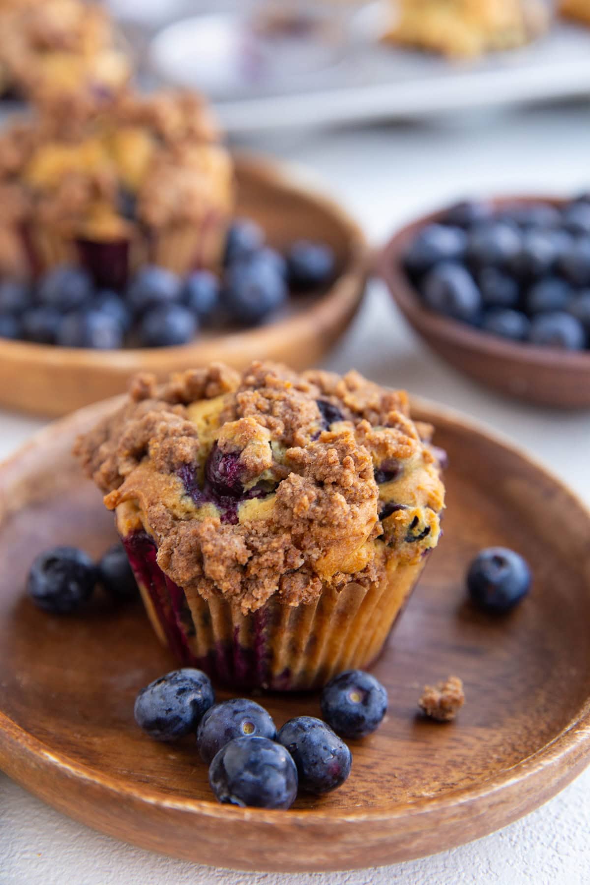 Two wooden plates with blueberry buttermilk muffins and fresh blueberries. A bowl of fresh blueberries in the background.