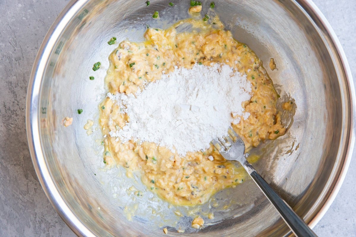 Mixing bowl with salmon patty ingredients with flour sprinkled on top, to be mixed in.