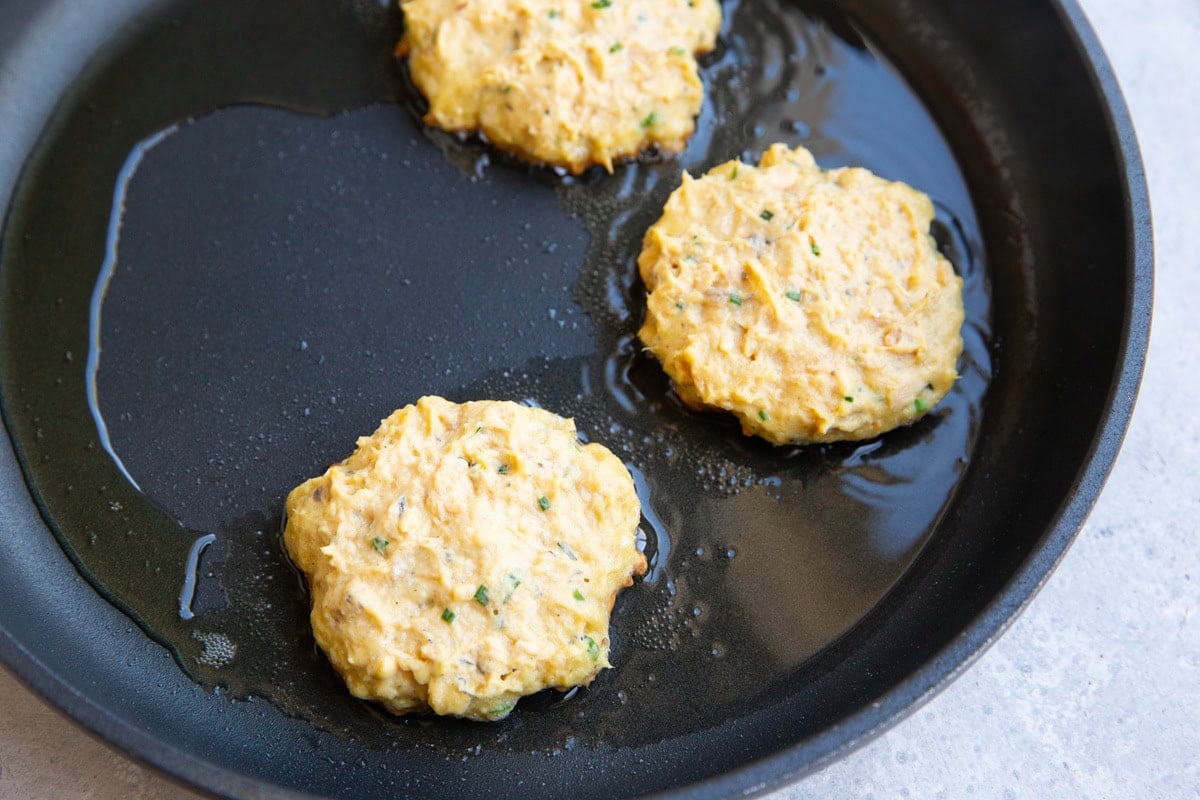Large skillet with three salmon patties cooking in oil.