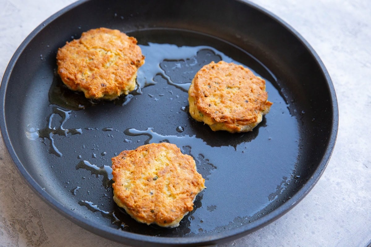 Large skillet with three golden brown salmon patties cooking in oil, finished and ready to serve.