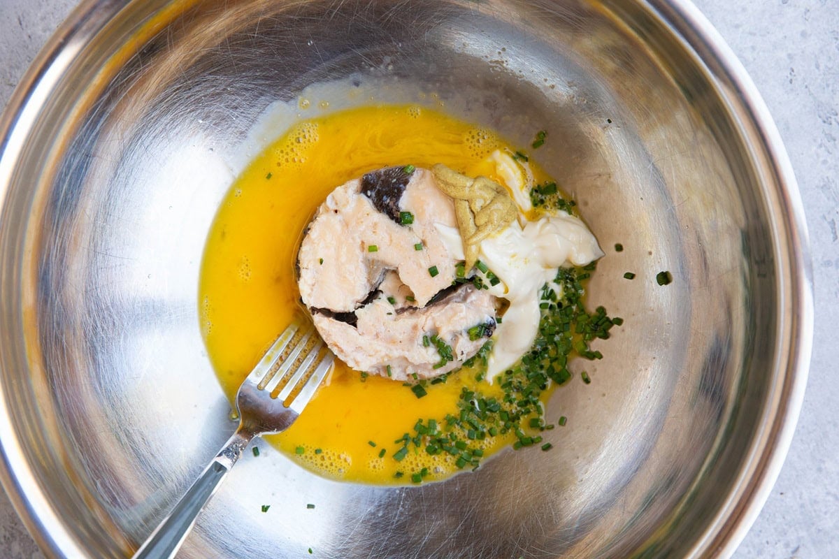 Ingredients for salmon patties in a large stainless steel bowl with a fork, to be mixed together.