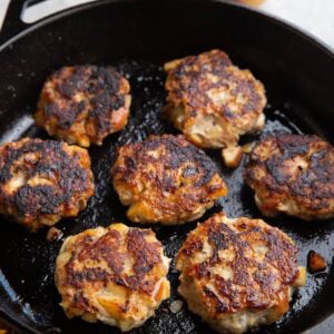 Cast iron skillet with seven chicken sausage patties and an apple in the background