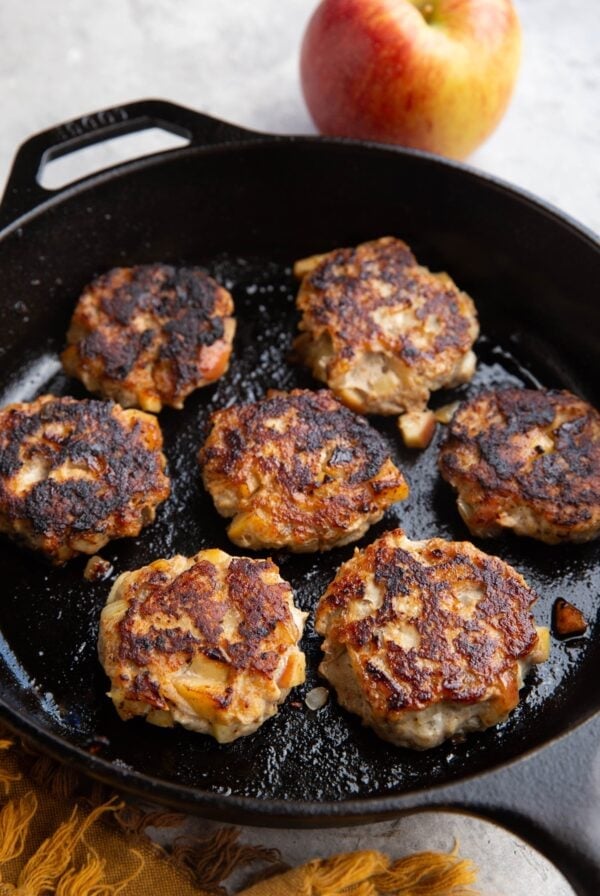 Cast iron skillet with seven chicken sausage patties and an apple in the background