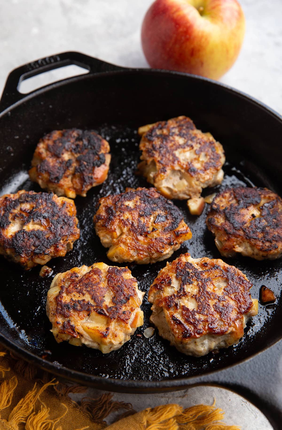 Cast iron skillet with seven chicken sausage patties and an apple in the background