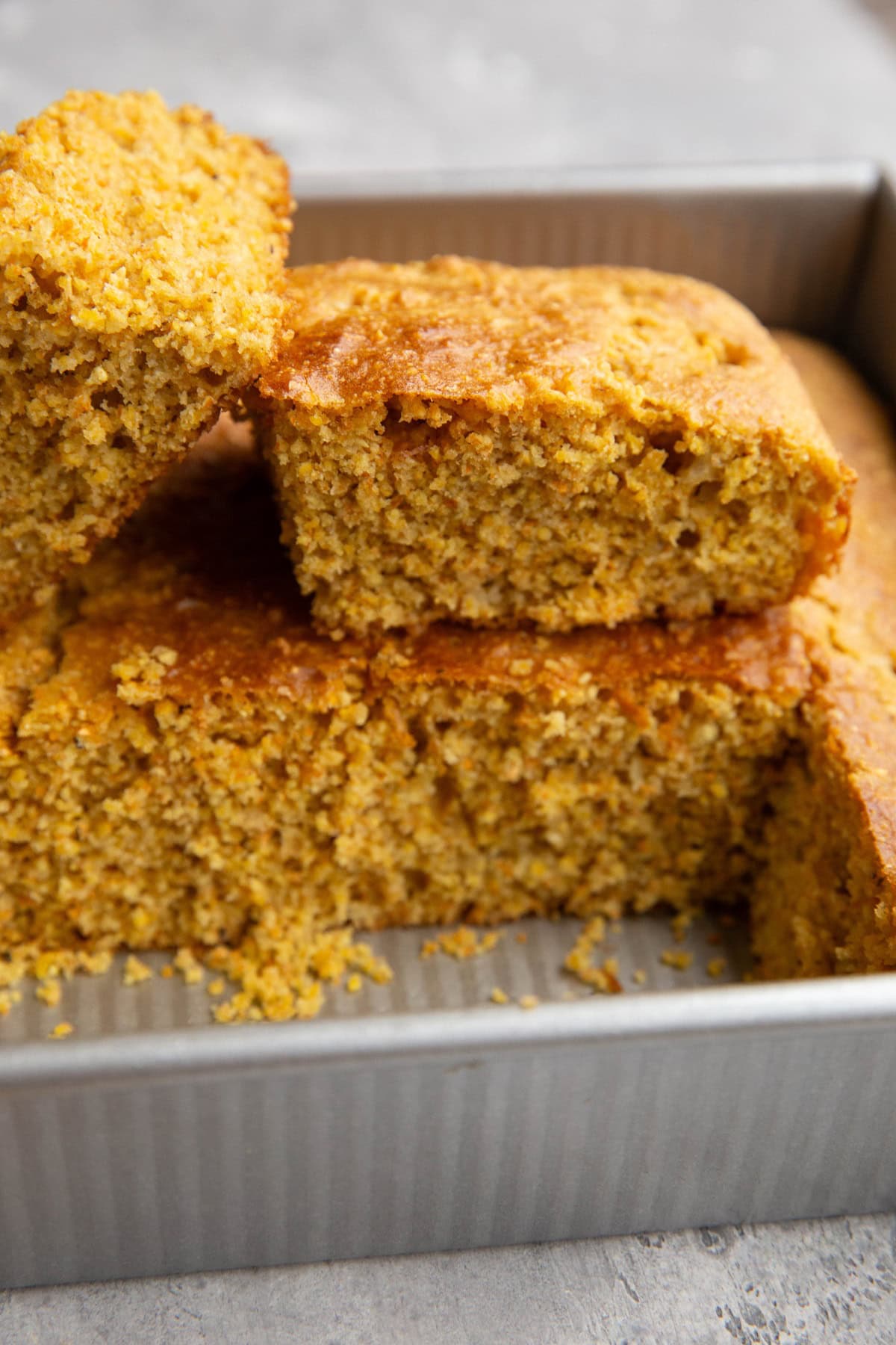 Baking dish of cornbread with two slices cut out and set on top to see the inside of the bread.