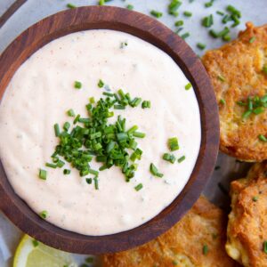 Wooden bowl full of crab cake sauce sitting on a plate next to freshly made salmon cakes and a slice of lemon - ready to serve.