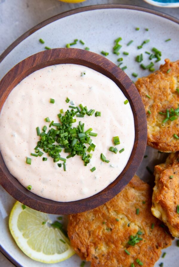 Wooden bowl full of crab cake sauce sitting on a plate next to freshly made salmon cakes and a slice of lemon - ready to serve.