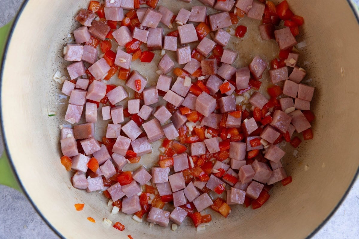 Large pot with chopped ham and bell peppers cooking.