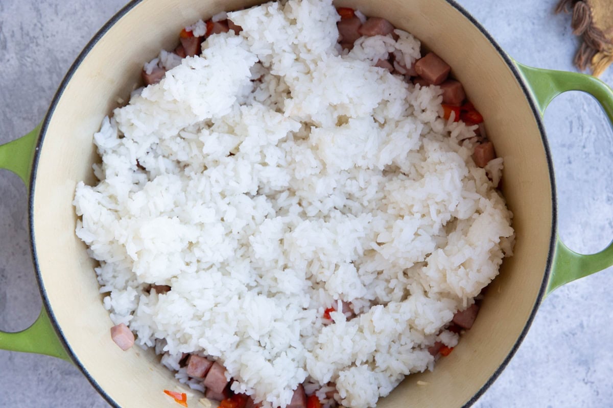 Large pot with bell pepper, chopped ham, and garlic on the bottom and cooked white rice added on top to be mixed in.
