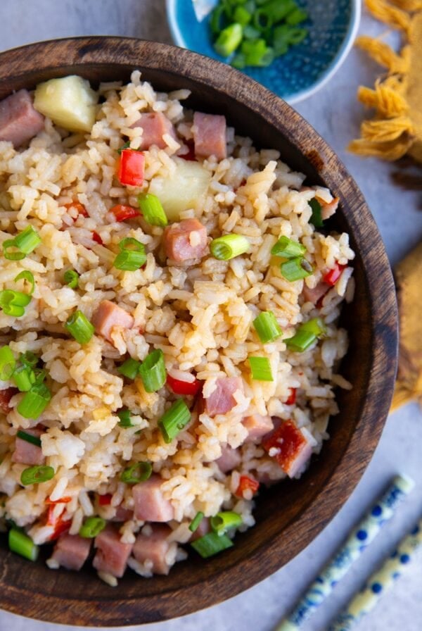large wooden bowl full of Hawaiian rice with a bowl of chopped onions and chop sticks to the side.