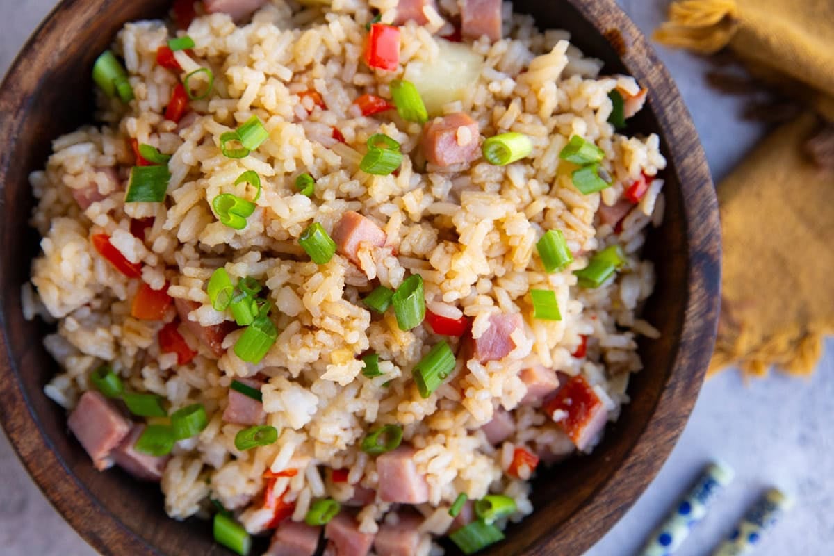 Hawaiian fried rice in a large wooden bowl with a golden napkin and chop sticks to the side.